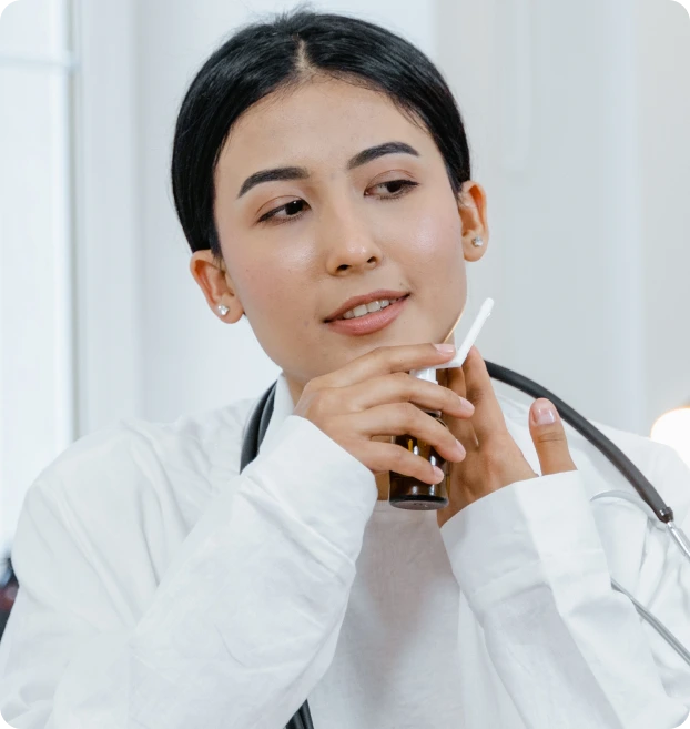 A healthcare professional in a white coat with a stethoscope around their neck holds a small brown bottle and a dropper, focusing on medication administration. The image highlights precision in home healthcare.