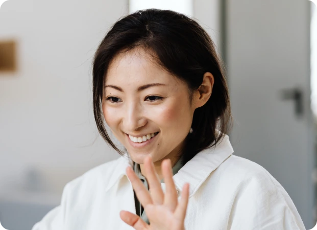 A healthcare professional in a white coat waves warmly in a clinical setting, creating a welcoming atmosphere. The image emphasizes friendly patient care and approachable medical services in a home environment.