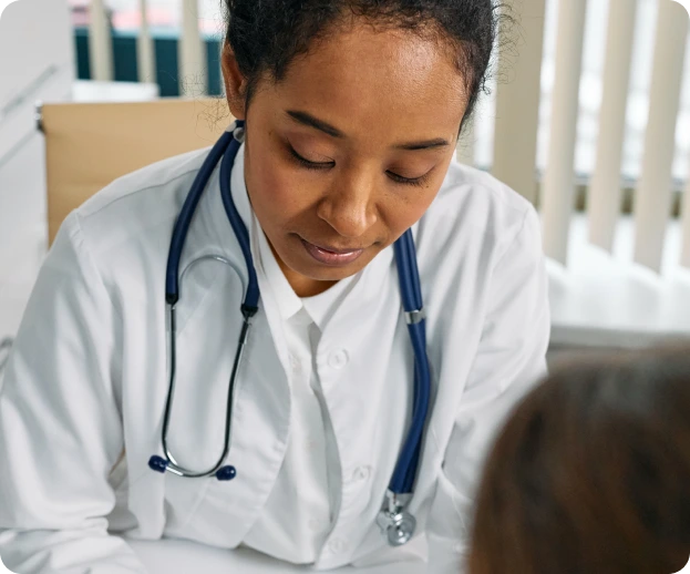 A female doctor with a stethoscope around their neck attentively examines a patient in a clinical setting. The image highlights focused patient care and medical consultations in a home environment