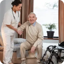 A nurse assists an elderly patient in a hospital room during post-operative care, helping him sit up on the bed with a wheelchair nearby. The image highlights compassionate healthcare and recovery support after surgery.