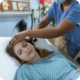 A nurse in a blue uniform gently checks a patient's head while they rest in a hospital bed at home. The image highlights post-operative recovery at home with professional healthcare support for healing and comfort.