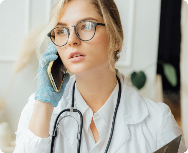 A Doctor wearing blue gloves and a stethoscope speaks on the phone in a medical setting. The image highlights at-home healthcare consultations for patient care.