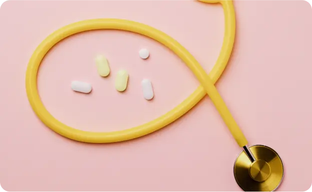 A yellow stethoscope with its tubing coiled into a circular shape on a pink background, surrounding several white and yellow pills of varying shapes and sizes. The stethoscope's chest piece is positioned at the bottom right, symbolizing healthcare and medical care, featured on the Intelligent Care website, a homecare service based in Dubai.